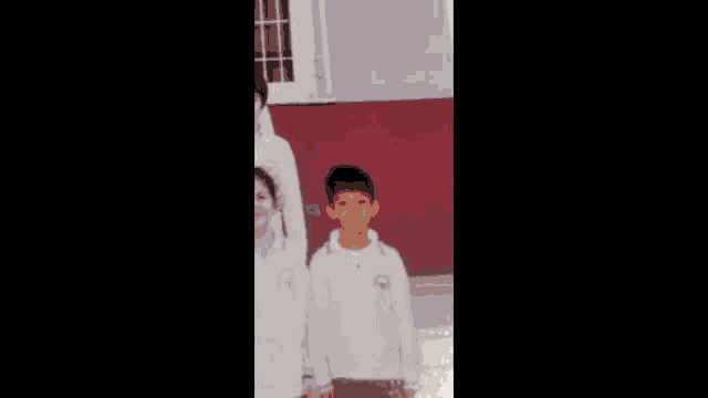 a young boy in a school uniform is standing in front of a red building .