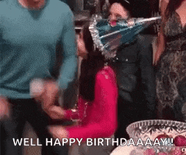 a woman wearing a party hat is sitting at a table with a plate of food .