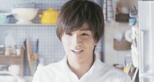 a young man in a white shirt is standing in a kitchen smiling at the camera .