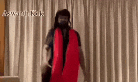a man is standing in front of a white curtain holding a red pillow .