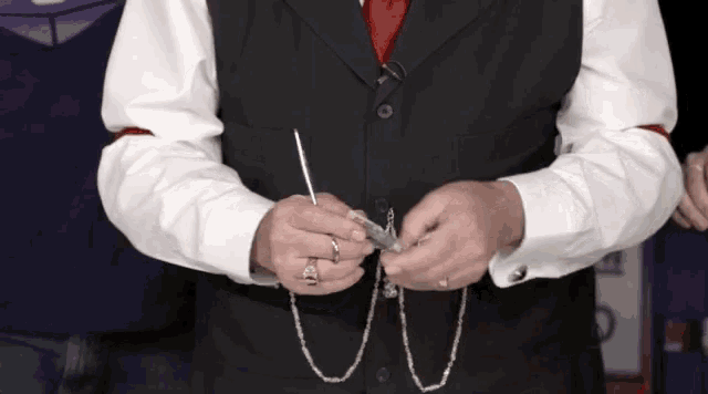 a man wearing a black vest and a red tie is holding a silver chain