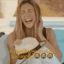 a woman is laughing while holding a hat and sunglasses .