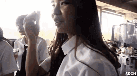 a girl in a white shirt and black tie is standing in a room with other people .