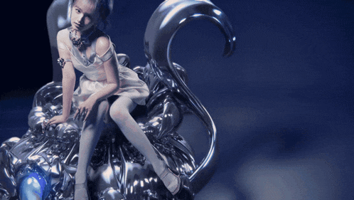 a woman in a white dress is sitting on a silver sculpture