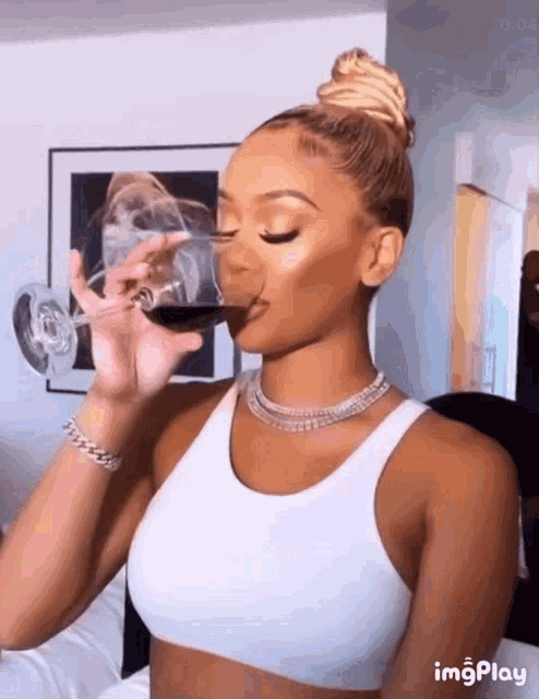 a woman in a white tank top is drinking from a wine glass ..
