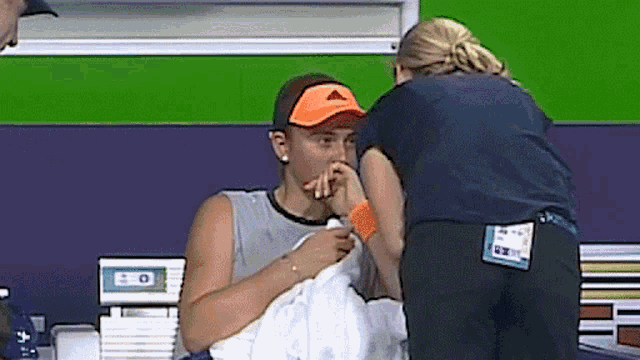 a woman wearing an orange adidas hat is being helped