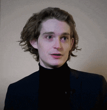 a young man with long hair is wearing a black turtleneck and a blue suit .