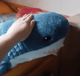 a person is petting a blue stuffed whale on a bed