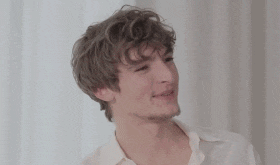 a young man with curly hair is smiling and looking at the camera while wearing a white shirt .