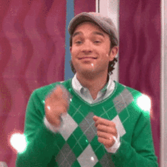a man wearing a green sweater and hat is clapping his hands