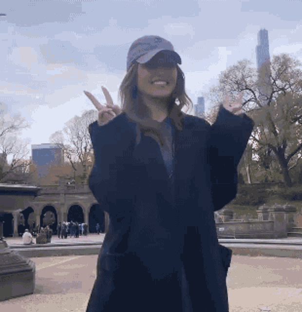 a woman wearing a hat and a black coat is giving the peace sign
