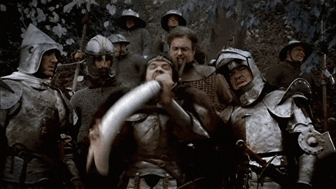 a group of medieval soldiers are standing around a man in armor holding a horn .