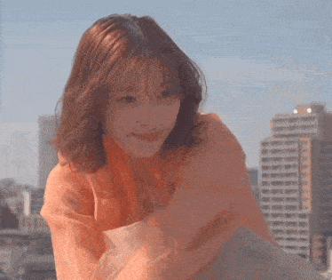 a woman in an orange shirt is sitting on a rooftop