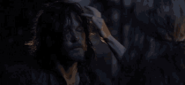 a woman is touching a man 's forehead in the dark in a dark room .