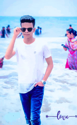 a man wearing sunglasses and a white shirt stands on a beach with the word love below him