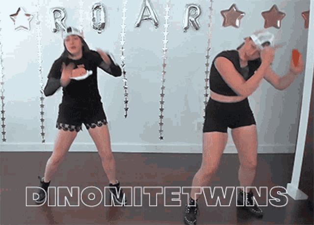 two women are dancing in front of a wall that says roar