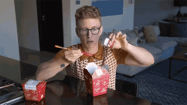 a man sitting at a table eating chinese food with chopsticks and a bottle that says ' noodles ' on it