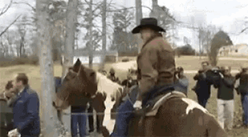 a man in a hat is riding a horse in a field with a crowd watching .