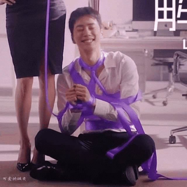 a man is tied up with a purple ribbon and sitting on the floor