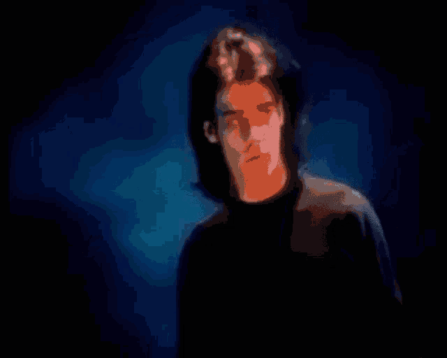 a man with long hair is standing in front of a blue background and looking at the camera .
