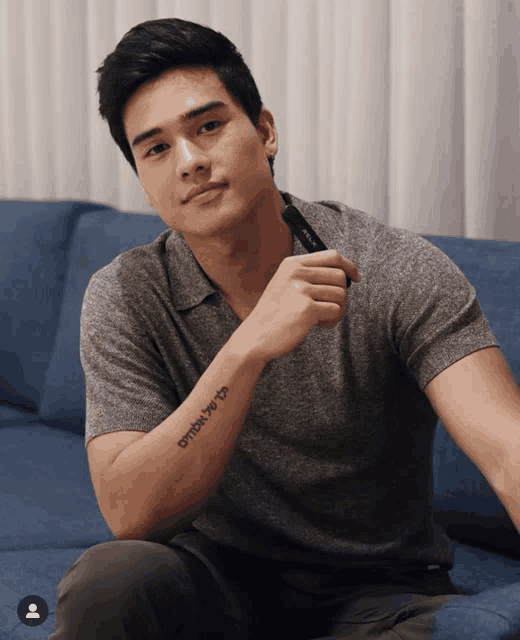 a man sitting on a couch with a tattoo on his arm that says " ombat be to "