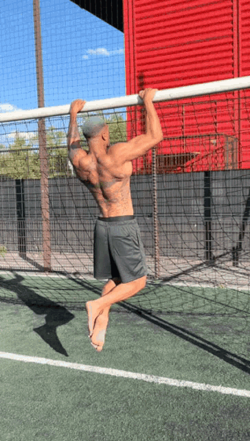 a man with tattoos on his back is doing a pull up