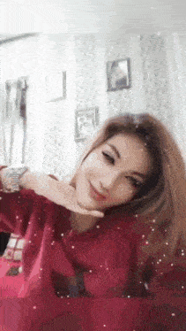 a woman wearing a red sweater and a watch is sitting in a room with her hands on her face .