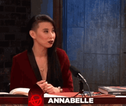 a woman in a red jacket is sitting in front of a microphone with the name annabelle above her