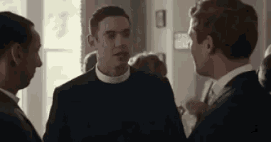 a group of men are standing next to each other in a room talking to each other .