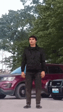 a man in a black jacket stands in front of a red police car