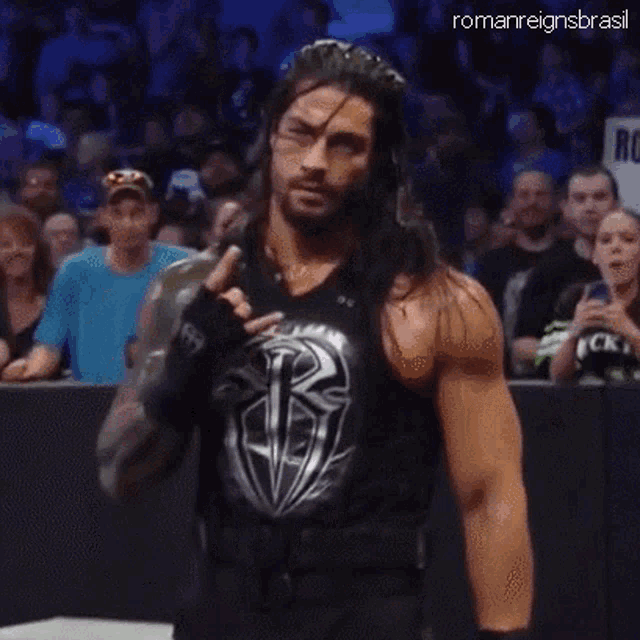 roman reigns is wearing a black tank top and giving a middle finger .