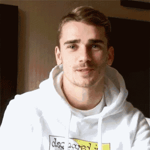 a young man wearing a white hoodie with a yellow sticker on it is looking at the camera .