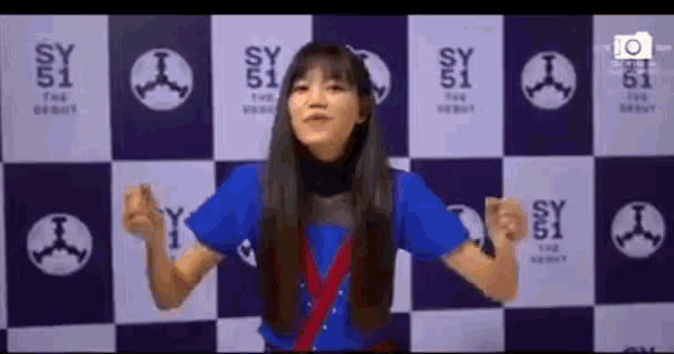 a woman in a blue shirt stands in front of a checkered wall with sy 51 on it