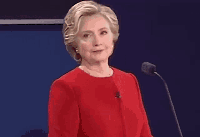 hillary clinton is giving a speech in front of a microphone while wearing a red shirt .