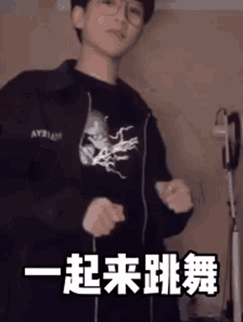 a young man wearing glasses is dancing in a room with chinese writing on the wall .