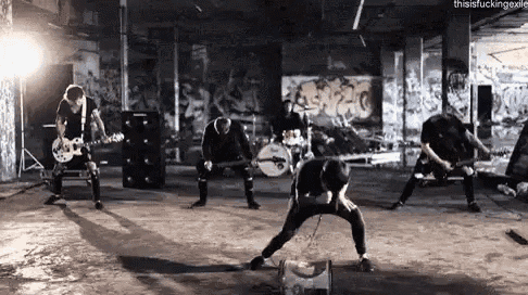 a group of men are playing guitars and drums in a room with graffiti on the walls .