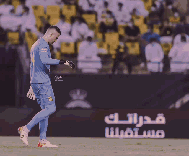 a soccer player stands on the field in front of a sign that says ' saudi arabia ' on it
