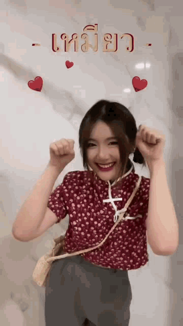 a woman in a red shirt is smiling in front of a wall with hearts and the words " เท ม ย ว "
