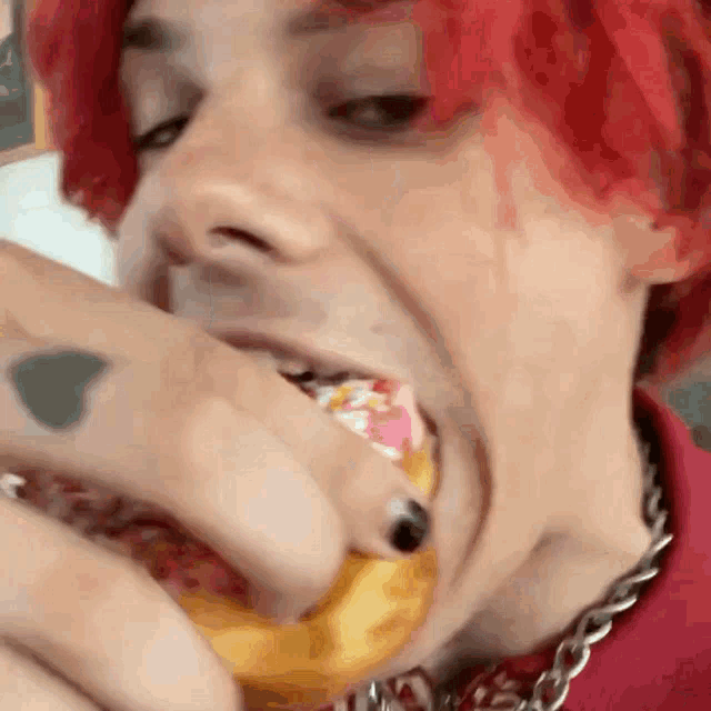 a person with red hair is eating a donut