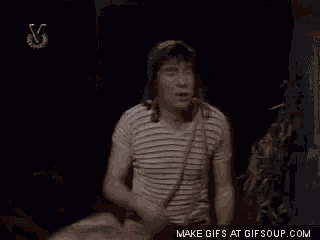a man wearing a hat and a striped shirt is dancing in a dark room .