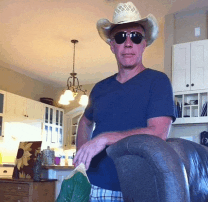 a man wearing a cowboy hat and sunglasses is sitting on a chair