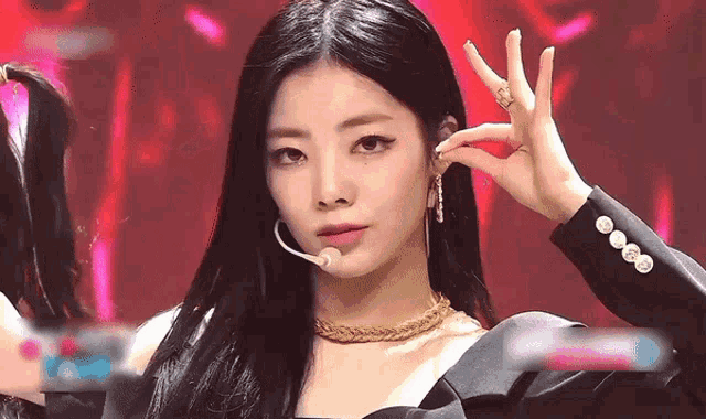 a woman with long black hair and a microphone in her ear is making a peace sign .