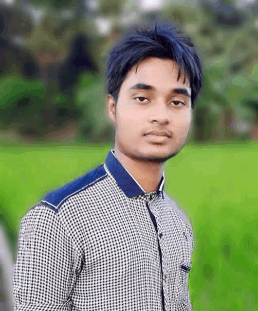 a young man wearing a plaid shirt is standing in front of a green field