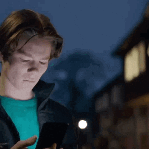 a man in a blue shirt is looking at a cell phone