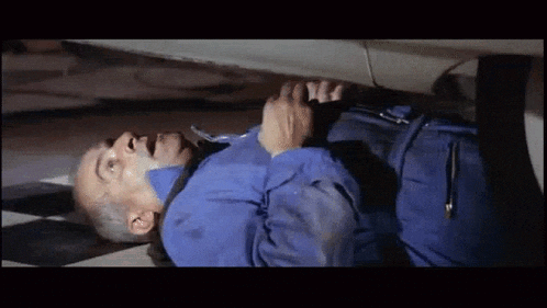 a man in a blue jumpsuit is laying on the floor under a car .