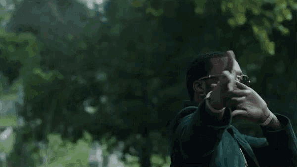a man wearing glasses and a green jacket is standing in a park .