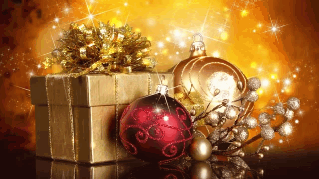 a gold gift box with a gold bow sits next to a red christmas ornament