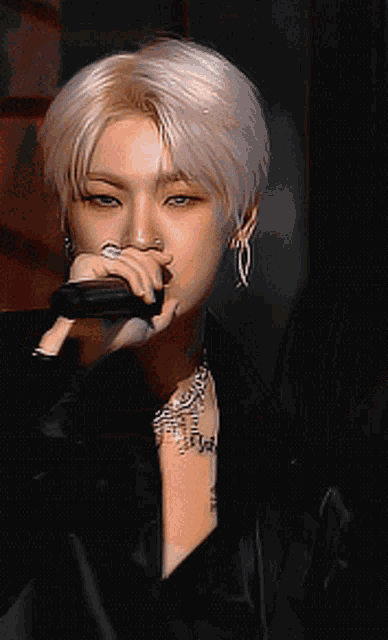 a young man is singing into a microphone while wearing a black jacket and a necklace