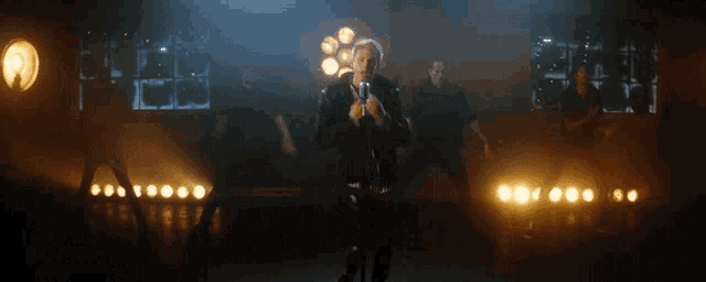 a man singing into a microphone with a group of people dancing in the background