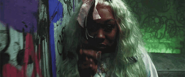 a woman with green hair is making a peace sign in front of a graffiti wall